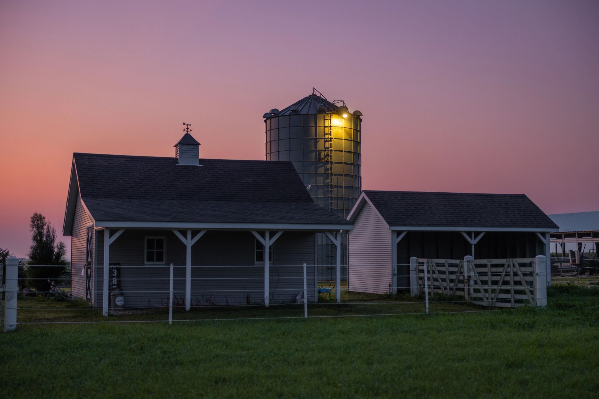 Los edificios de la granja y un silo iluminado en Hickory Hill Farms bajo un cielo rosado al atardecer